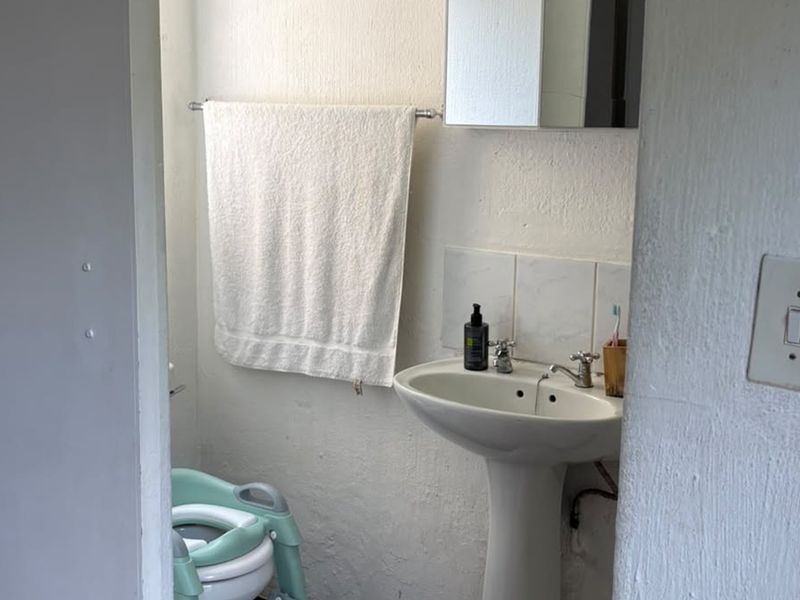 A compact bathroom featuring a pedestal basin, tiled splashback, and wall-mounted medicine cabinet, requiring cosmetic updates to the wall finishes.