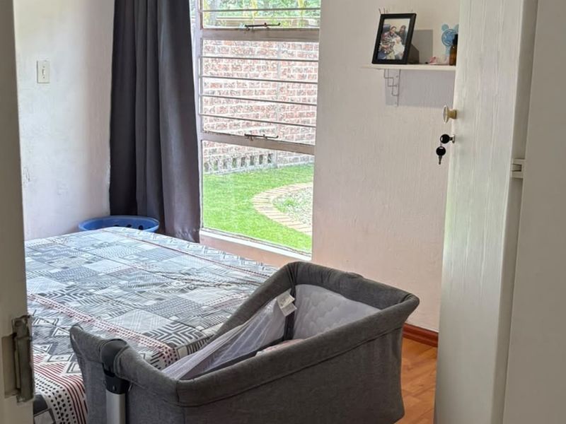 A bedroom featuring laminate flooring and a louvered window overlooking the garden area.