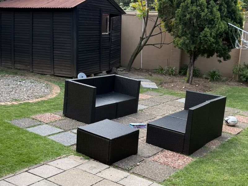 A private garden area featuring a lawn, paved seating section, and a timber storage shed enclosed by brick boundary walls.