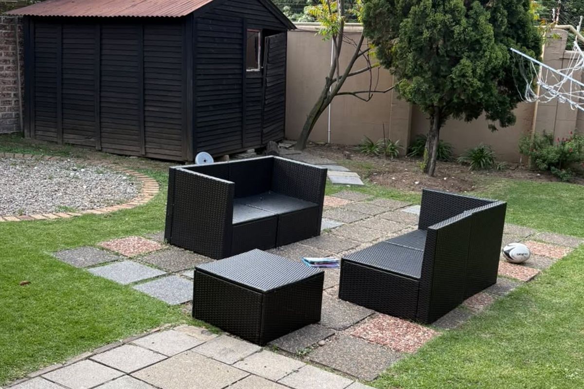 A private garden area featuring a lawn, paved seating section, and a timber storage shed enclosed by brick boundary walls.