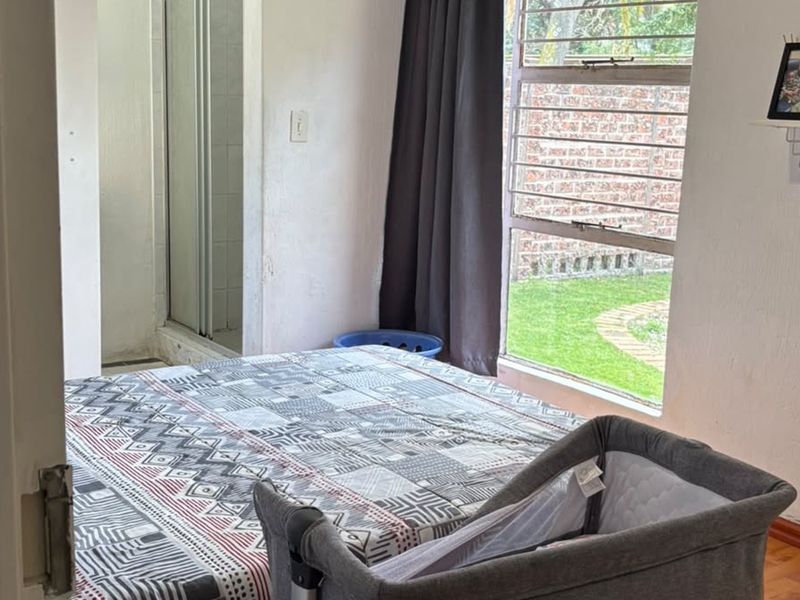 Bedroom featuring laminate flooring, a large window with security bars, and an attached en-suite shower area.