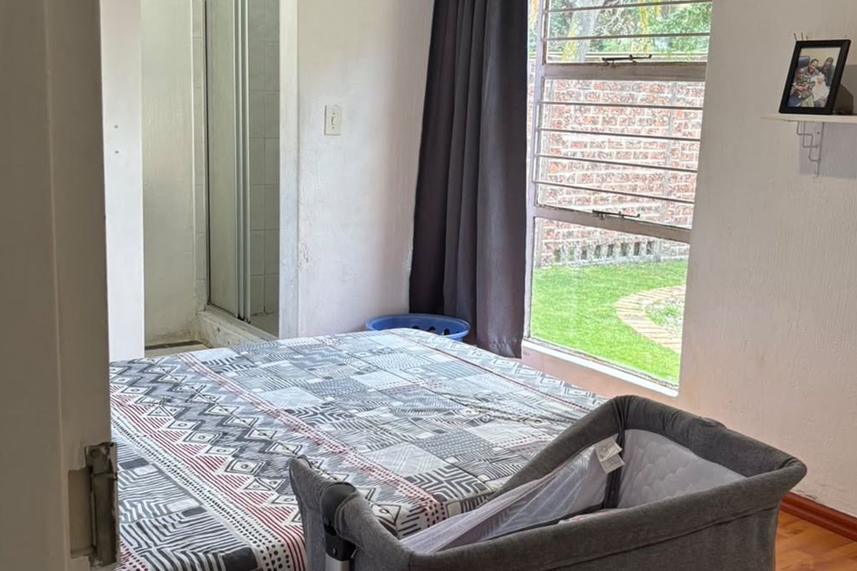 Bedroom featuring laminate flooring, a large window with security bars, and an attached en-suite shower area.