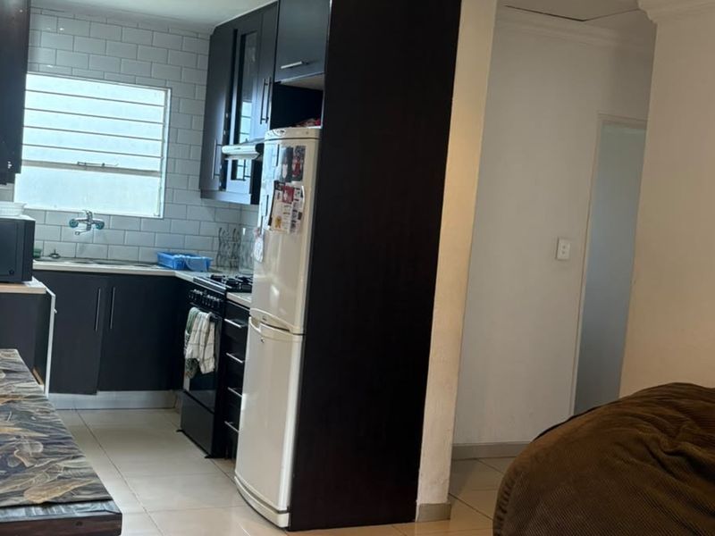 Open plan kitchen area featuring dark cabinetry, subway tile backsplash, and tiled flooring, seamlessly connecting to the adjacent living space.