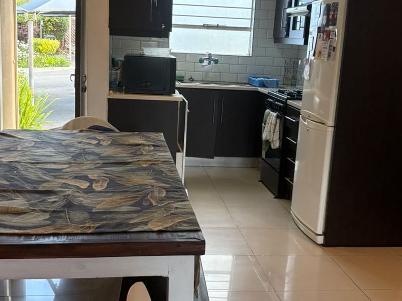 Open plan kitchen area featuring dark cabinetry, subway tile backsplash, and tiled flooring, with direct access to the outdoor space.