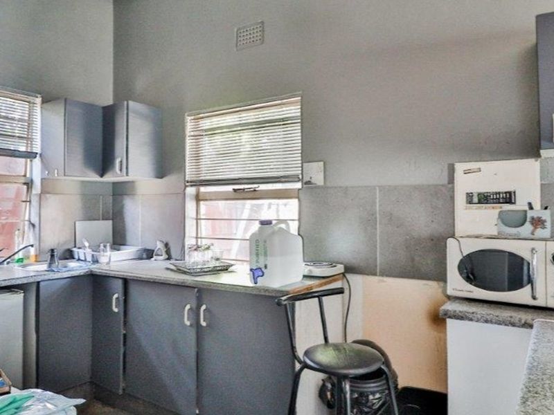 A compact kitchen featuring grey cabinetry, laminate countertops, and a tiled backsplash, currently showing signs of wear and requiring cosmetic updates.
