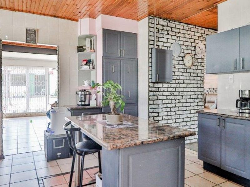 A kitchen featuring granite countertops, built-in cabinetry, an exposed brick feature wall, and a timber-clad ceiling, offering a blend of rustic and modern elements.