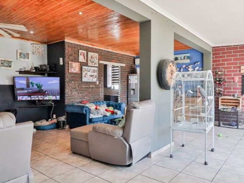 Open plan living area featuring tiled floors, a timber ceiling, exposed brick feature walls, and a built-in braai area.