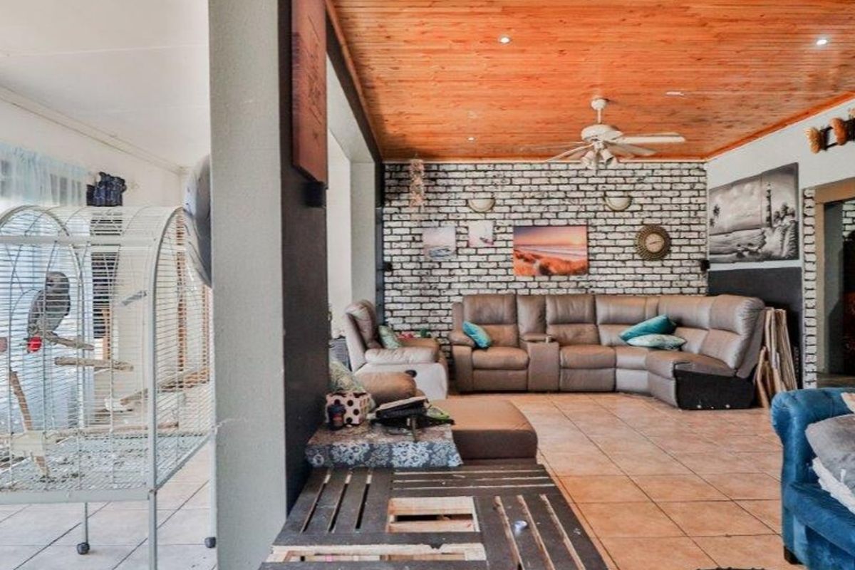 Spacious living area featuring a rustic exposed brick wall, warm timber ceiling, and tiled flooring, creating a comfortable and inviting atmosphere.