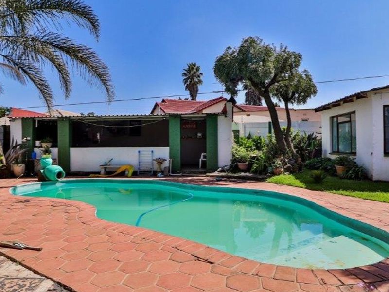 Outdoor pool area featuring a kidney-shaped swimming pool, paved surround, and a covered patio space, set within a private garden.