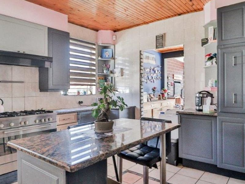 A functional kitchen featuring granite countertops, gas stove with extractor fan, ample built-in cabinetry, and a distinctive timber ceiling.
