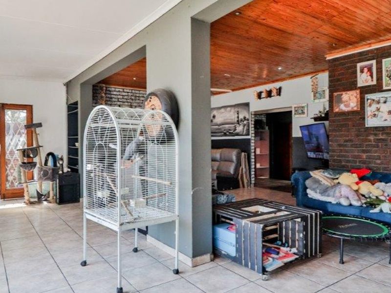 Open plan living area featuring tiled floors, exposed brick feature wall, and timber ceiling, providing a versatile space with direct access to the exterior.