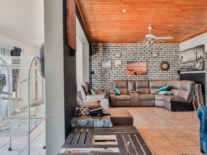 Spacious living area featuring a rustic exposed brick wall, warm timber ceiling with integrated lighting, and durable tiled flooring.