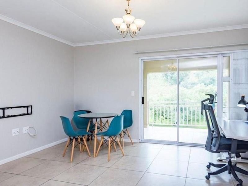 Open-plan living area featuring neutral tiled flooring, a wall-mounted TV bracket, and large sliding glass doors providing access to an outdoor balcony.