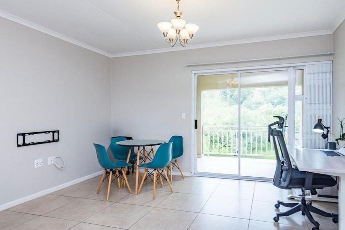 Open-plan living area featuring neutral tiled flooring, a wall-mounted TV bracket, and large sliding glass doors providing access to an outdoor balcony.