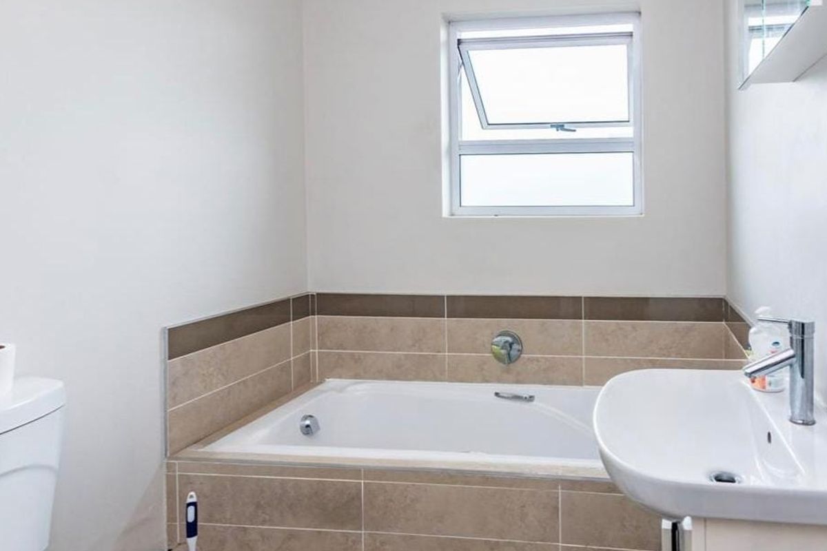 A clean and functional bathroom featuring a built-in bathtub with tiled surround, a pedestal washbasin, and a toilet.