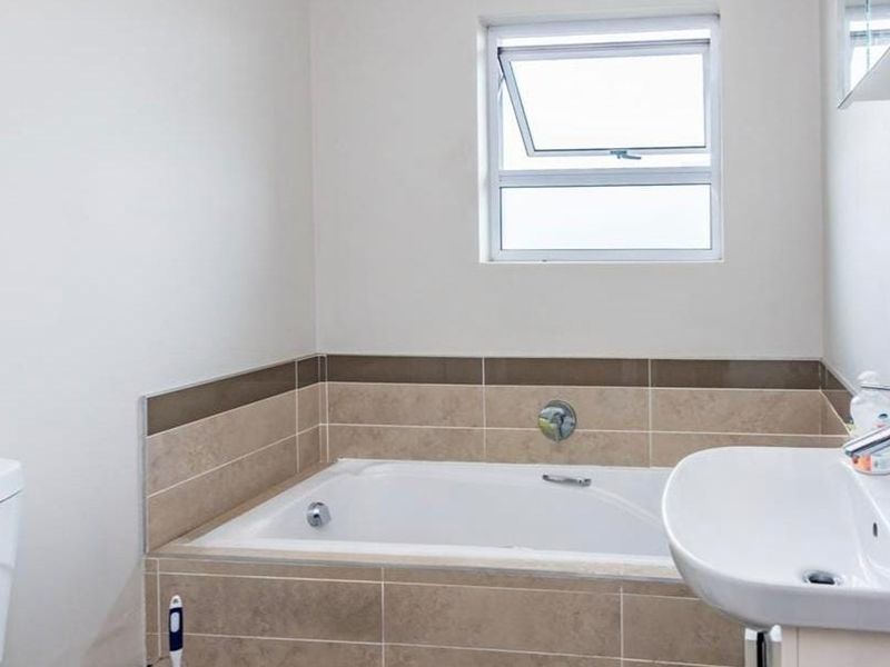 A clean and functional bathroom featuring a built-in bathtub with tiled surround, a pedestal washbasin, and a toilet.