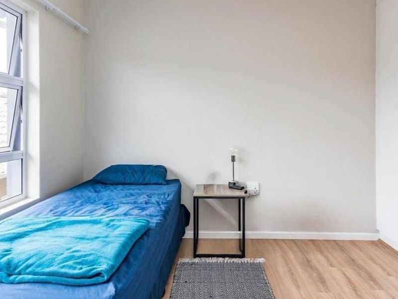 A bright bedroom featuring laminate flooring, a built-in wardrobe, and a large top-hung window providing natural light.