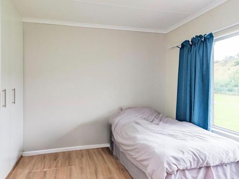 A functional bedroom featuring light-toned laminate flooring, neutral wall finishes, and ample built-in cupboard storage with a large window providing natural light.