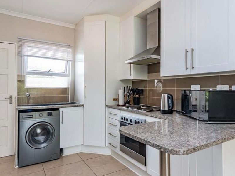 A functional kitchen featuring white cabinetry, granite countertops, a built-in oven with extractor fan, and integrated laundry plumbing.