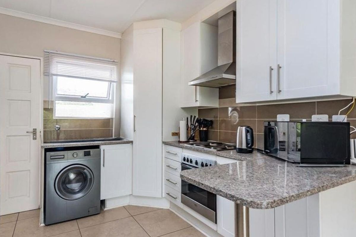 A functional kitchen featuring white cabinetry, granite countertops, a built-in oven with extractor fan, and integrated laundry plumbing.
