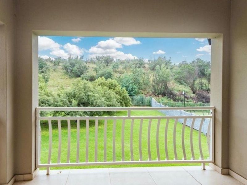 A covered balcony featuring tiled flooring and a white metal balustrade, offering an open view of the surrounding green landscape.