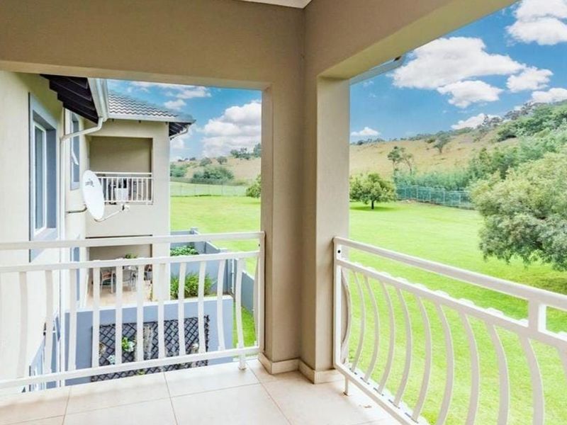 A covered balcony featuring tiled flooring and a white metal balustrade, offering scenic views of the surrounding green landscape.