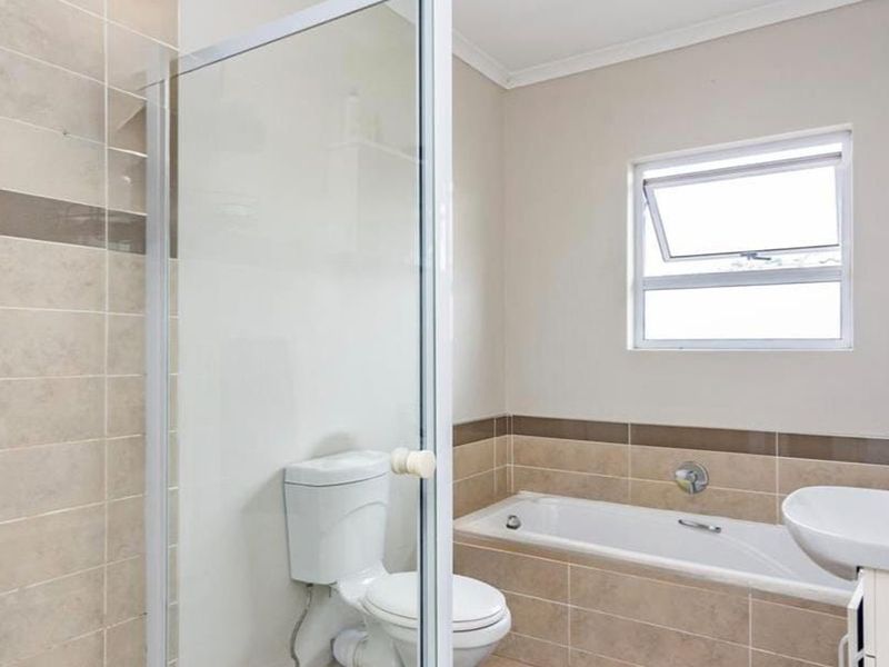A well-maintained bathroom featuring a shower enclosure, bathtub, basin, and neutral tiled finishes with a top-hung window for natural light.