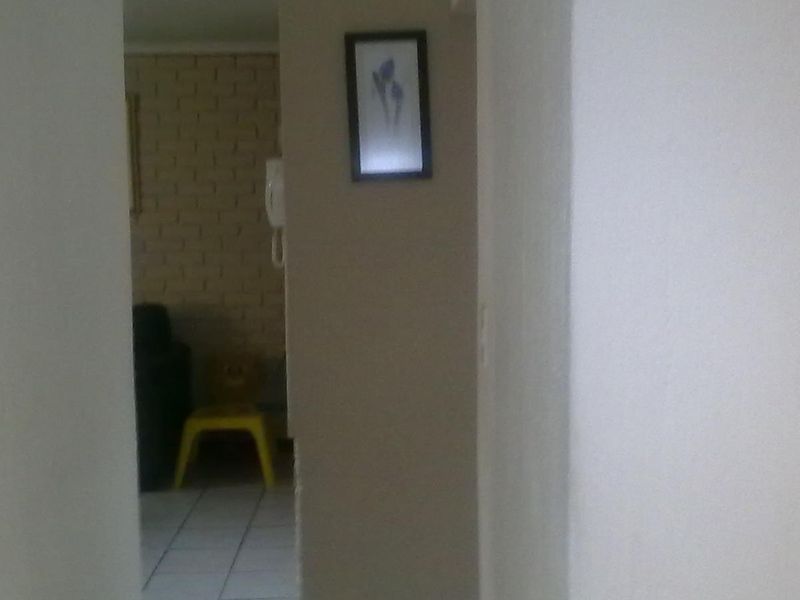 A view through a hallway showing an intercom system and electrical distribution board, leading into an adjacent living area with tiled flooring.