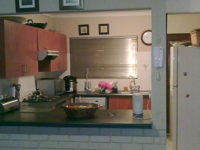 A functional kitchen featuring laminate cabinetry, dark countertops, a breakfast bar with a brick base, and a stainless steel sink.