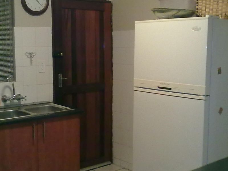 A functional kitchen area featuring wooden cabinetry, a double bowl stainless steel sink, and tiled splashbacks, offering a practical layout for daily use.