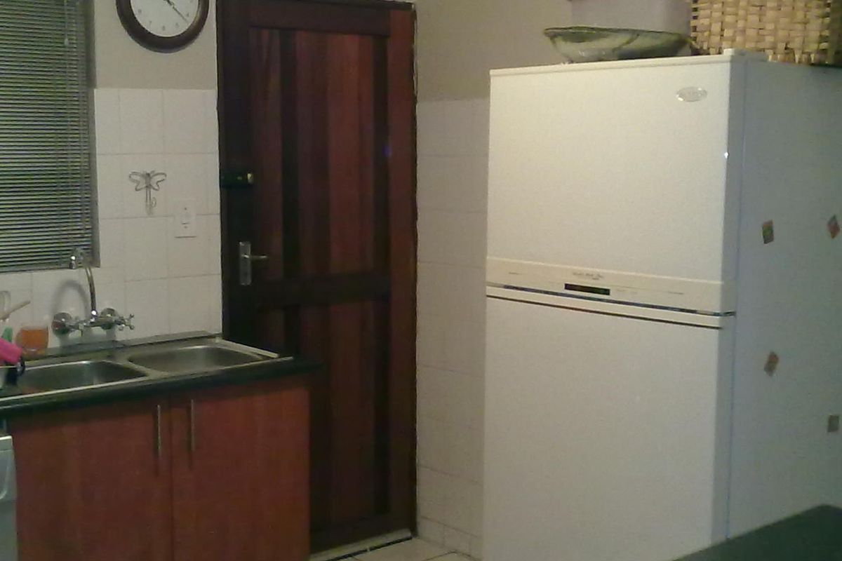 A functional kitchen area featuring wooden cabinetry, a double bowl stainless steel sink, and tiled splashbacks, offering a practical layout for daily use.
