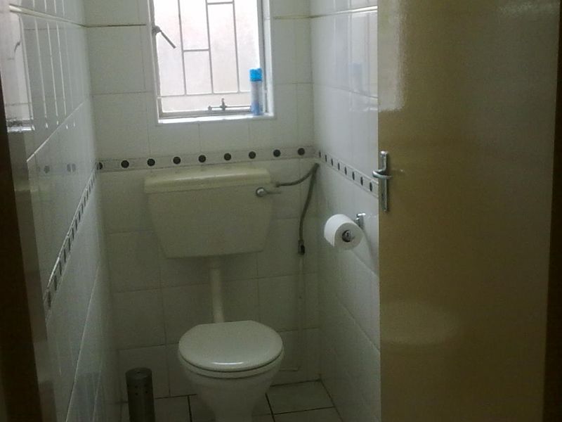 A compact, dated guest bathroom featuring white wall tiles with a decorative border, tiled flooring, and a standard toilet.