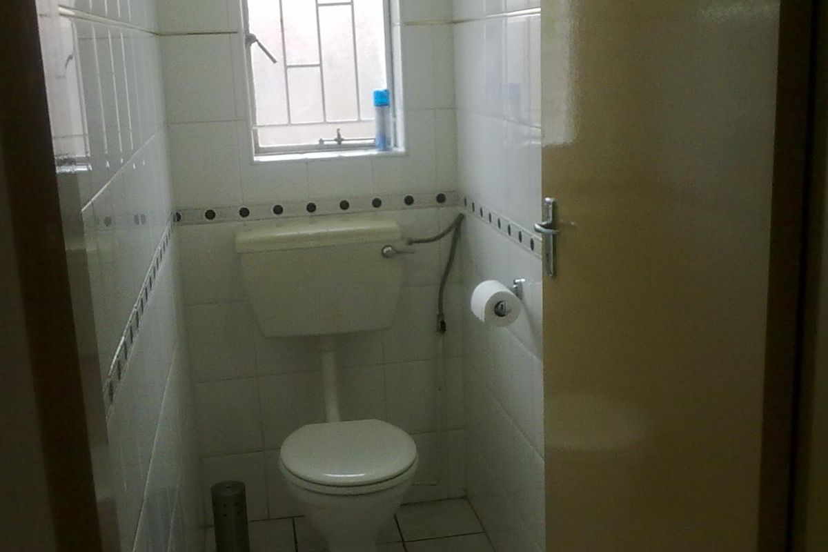 A compact, dated guest bathroom featuring white wall tiles with a decorative border, tiled flooring, and a standard toilet.