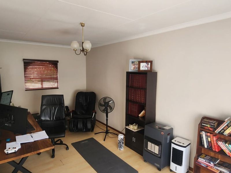A functional home office space featuring laminate flooring, a window with venetian blinds, and a central ceiling light fixture.
