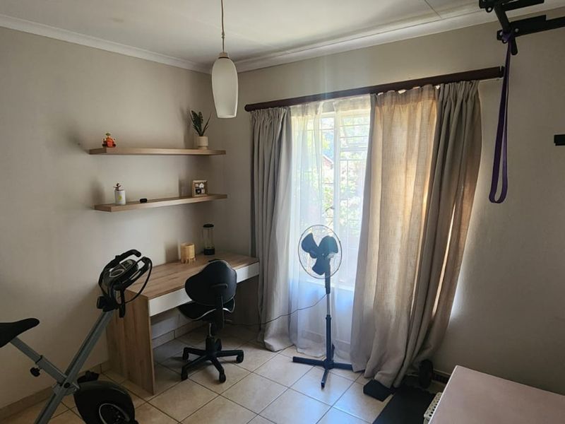 A functional home office space featuring tiled flooring, built-in wall shelving, and natural light through a window with curtain fixtures.