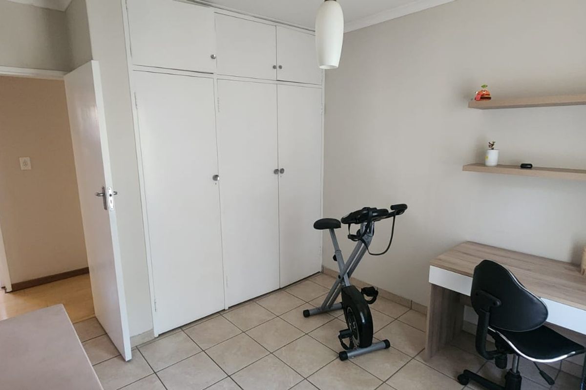 A functional bedroom featuring built-in cupboards, tiled flooring, and floating wall shelves, offering a practical space with neutral finishes.