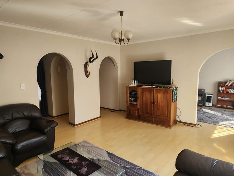Spacious living room featuring laminate flooring, coved cornicing, and distinctive arched doorways leading to adjacent areas.