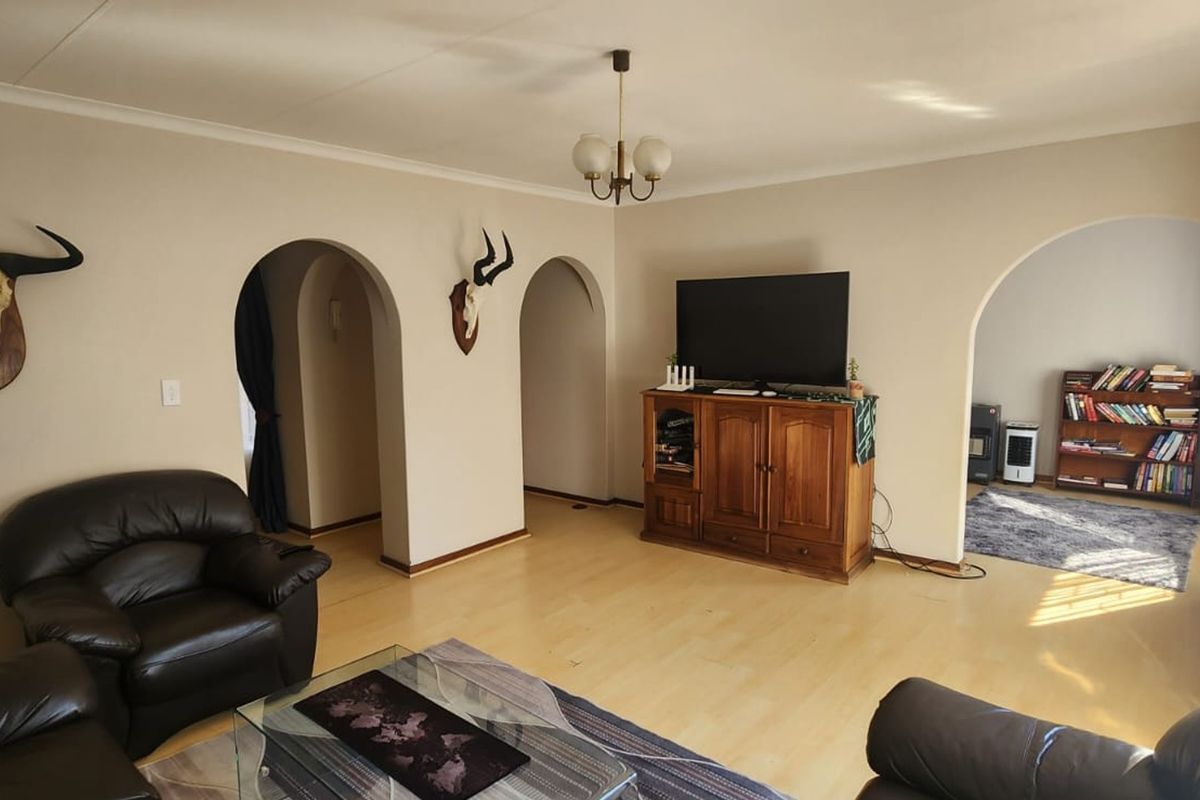Spacious living room featuring laminate flooring, coved cornicing, and distinctive arched doorways leading to adjacent areas.