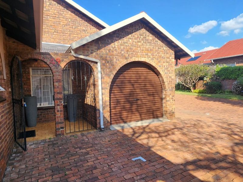 Front exterior view of a face brick townhouse featuring an arched garage door, secure entrance gate, and a paved driveway.