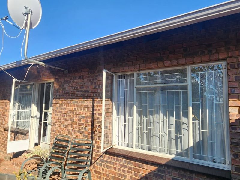Rear exterior view of a brick townhouse featuring security bars on windows and a satellite dish installation.