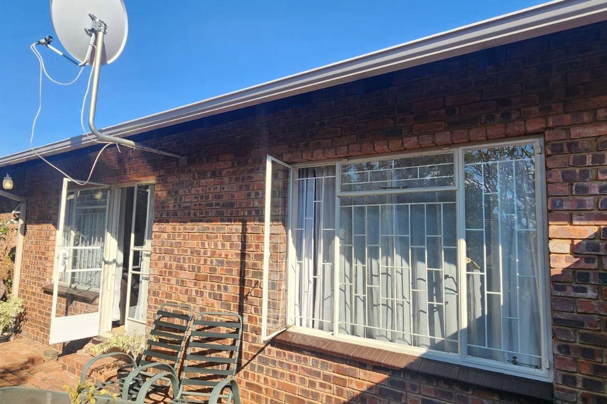 Rear exterior view of a brick townhouse featuring security bars on windows and a satellite dish installation.