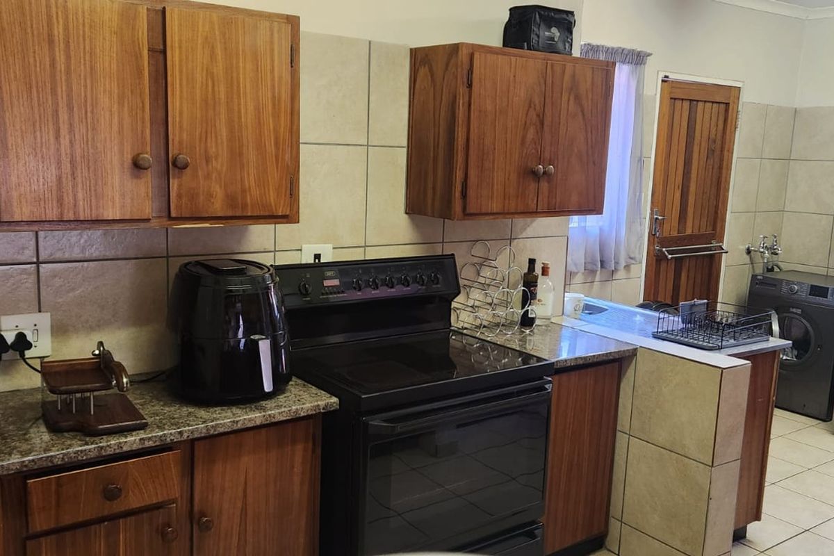 A functional kitchen featuring wooden cabinetry, granite countertops, tiled backsplash, and an integrated electric stove, with an adjacent laundry area.