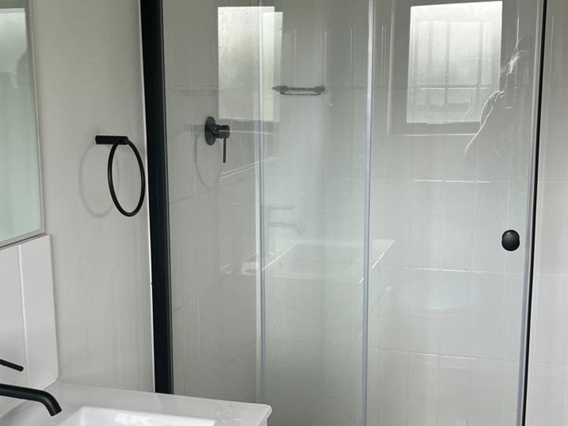 Modern bathroom featuring a glass shower enclosure with black fixtures, a vanity basin with a black mixer tap, and clean white wall tiling.