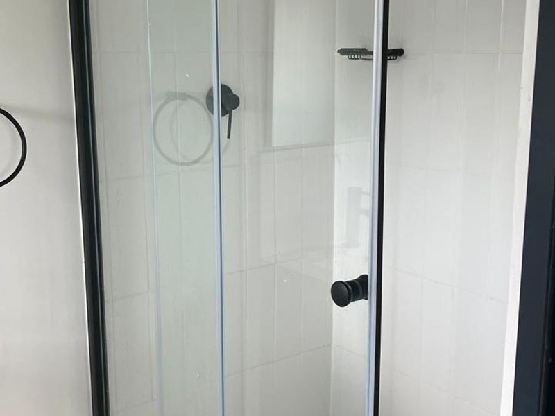 A modern bathroom shower featuring a sleek black frame, matching black fixtures, and clean white wall tiling.