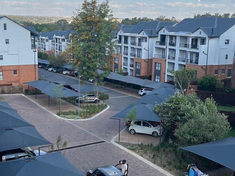 An elevated view of a modern apartment complex featuring paved driveways, numerous shade cloth carports, and well-maintained multi-story residential buildings.