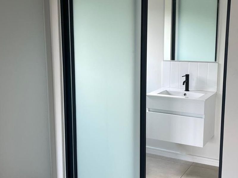 A modern, minimalist bathroom featuring a wall-mounted vanity with a sleek black mixer tap, tiled splashback, and a sliding frosted glass door.