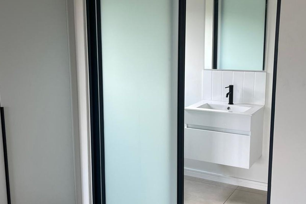 A modern, minimalist bathroom featuring a wall-mounted vanity with a sleek black mixer tap, tiled splashback, and a sliding frosted glass door.