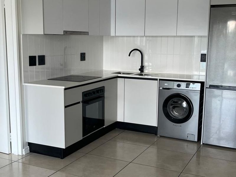 Modern kitchen featuring white cabinetry, quartz countertops, tiled backsplash, integrated oven and hob, and tiled flooring in a clean, contemporary layout.