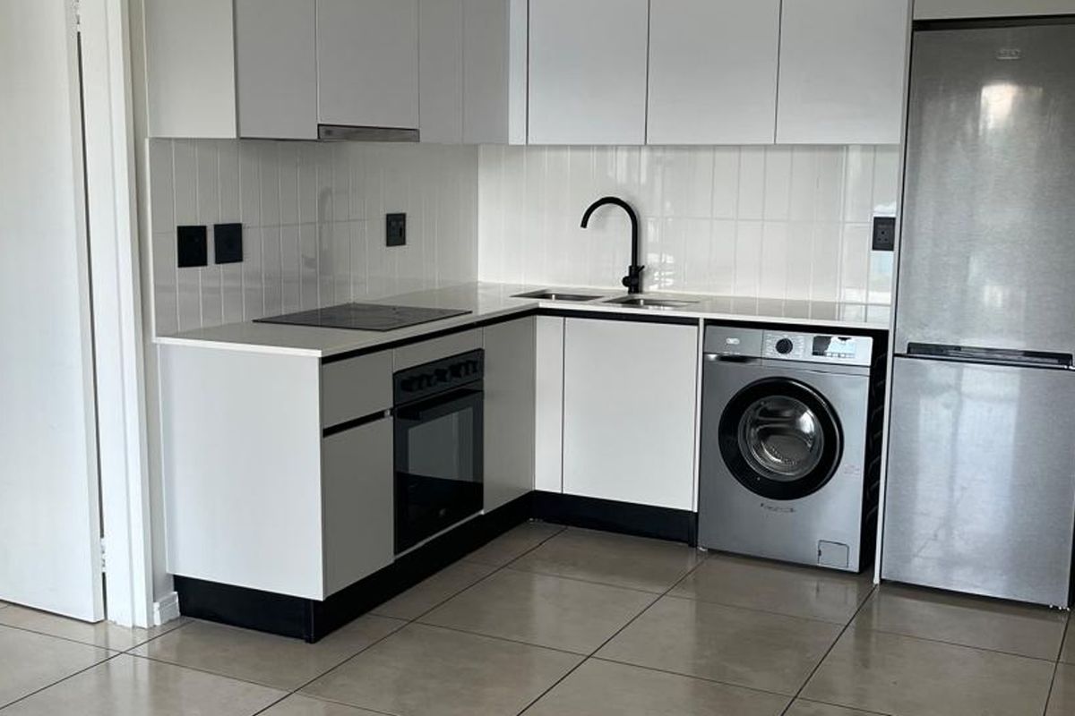 Modern kitchen featuring white cabinetry, quartz countertops, tiled backsplash, integrated oven and hob, and tiled flooring in a clean, contemporary layout.