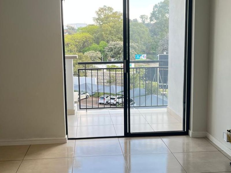 An empty living area featuring large sliding glass doors that open onto a private balcony with tiled flooring.
